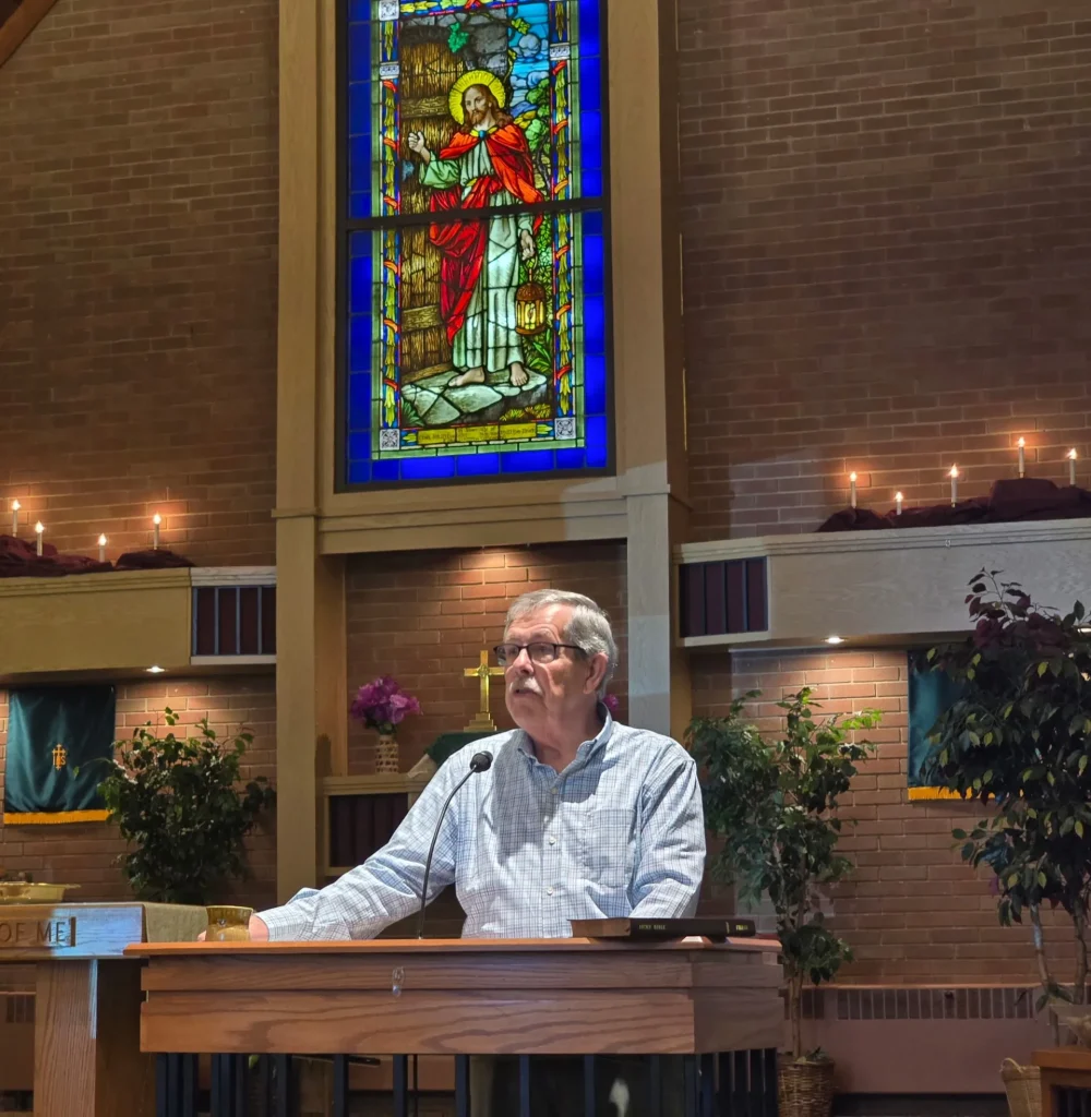 A speaker at the lectern beneath the sanctuary's stained-glass window